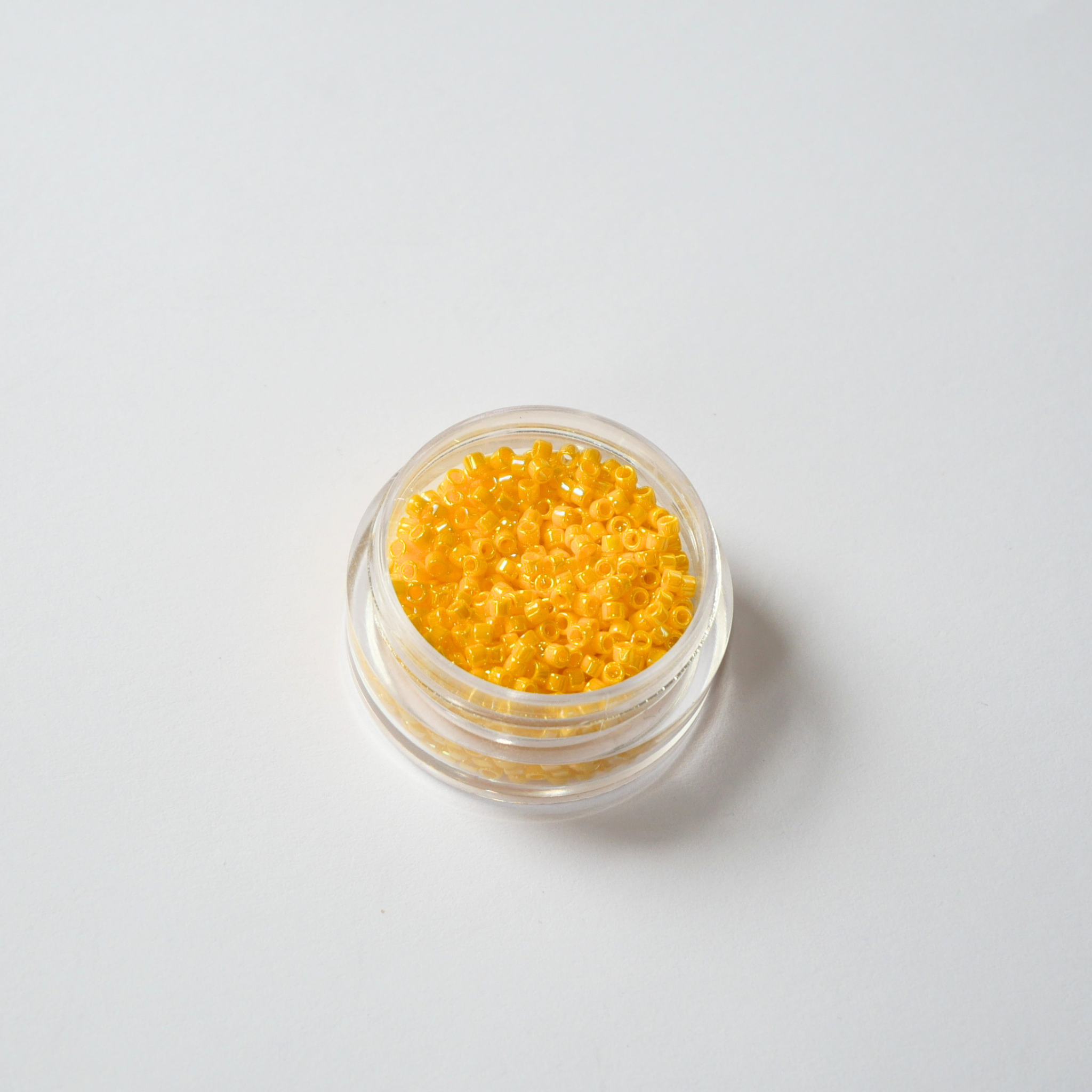Miyuki Delica 11/0 koodiga DB-1572. Detailne lähivõte läbipaistmatutest kanaarikollastest vikerkaarelise AB-läikega (Opaque Canary AB) silindrilistest helmestest.