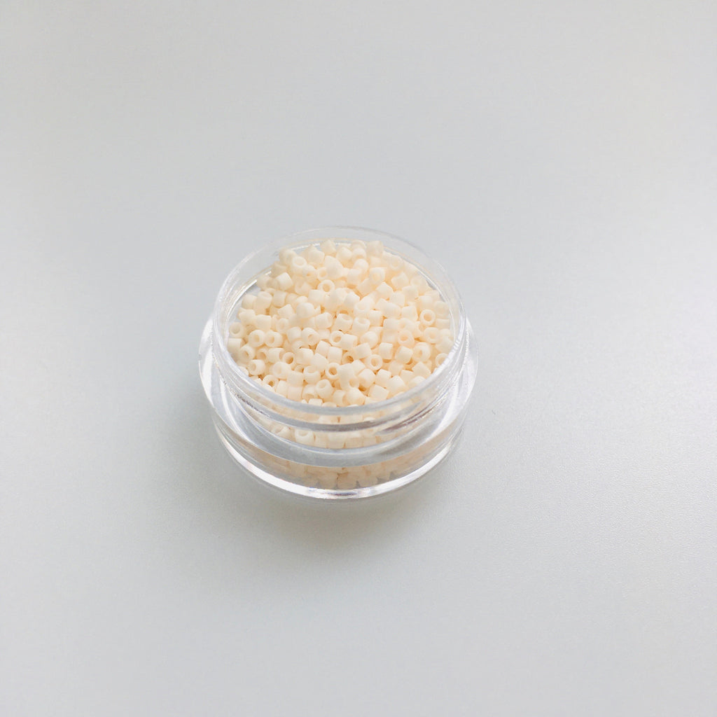 Miyuki Delica 11/0 DB-1510 Opaque Bisque White Mat silindrilised seemnehelmed. Lähivõte näitab sametist matt kreemjasvalget tooni, mis sobib hästi vintage-stiili.