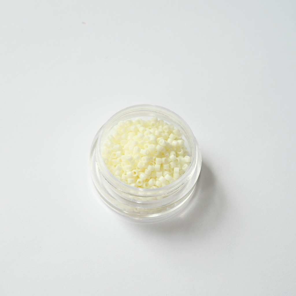 Miyuki Delica 11/0 koodiga DB-2401. Detailne lähivõte läbipaistmatutest soojadest kreemikasvalgetest (Opaque Light Buttercream) silindrilistest helmestest.
